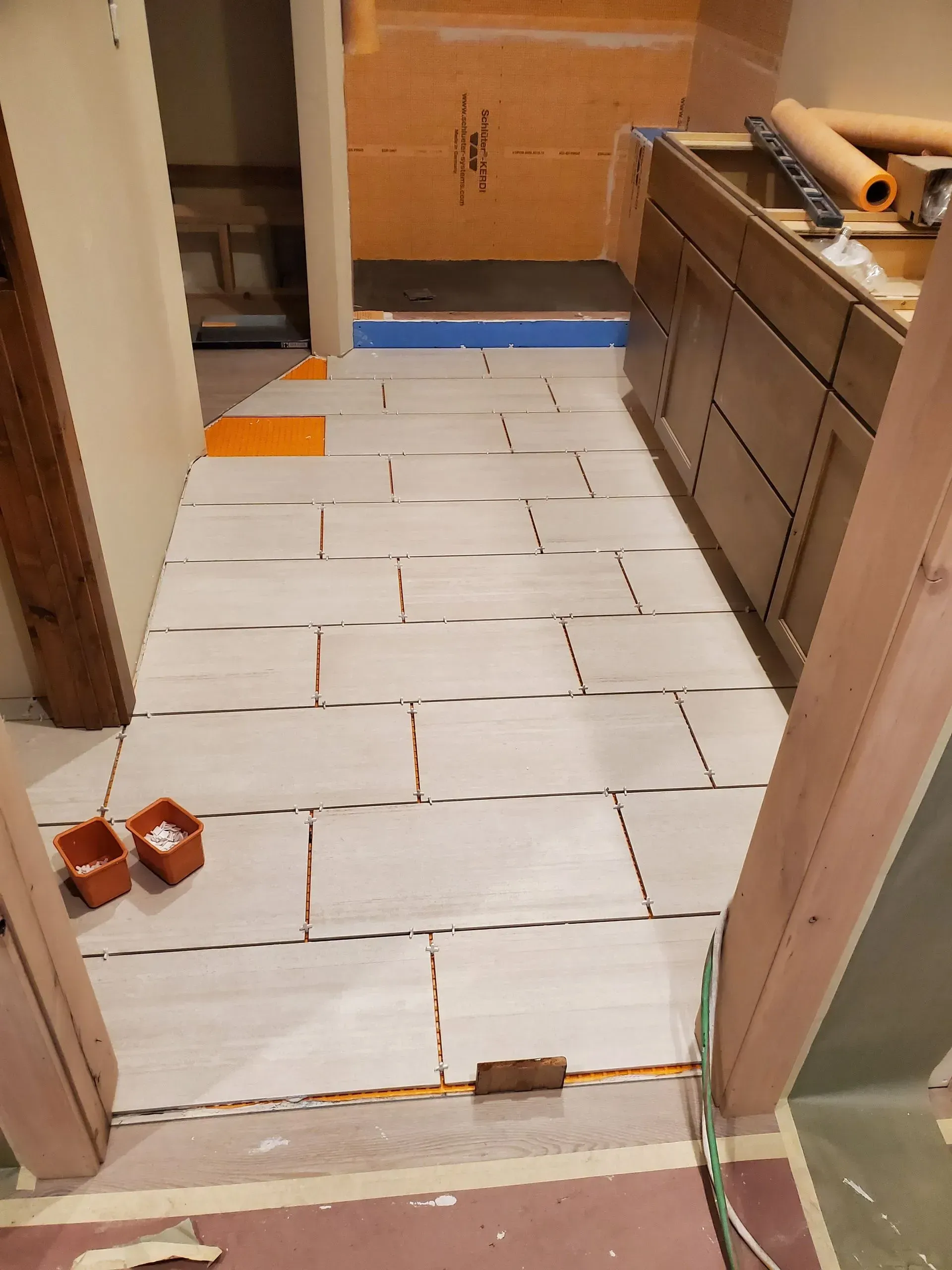 Partially tiled hallway floor under construction, with white tiles, blue tape, and tools nearby