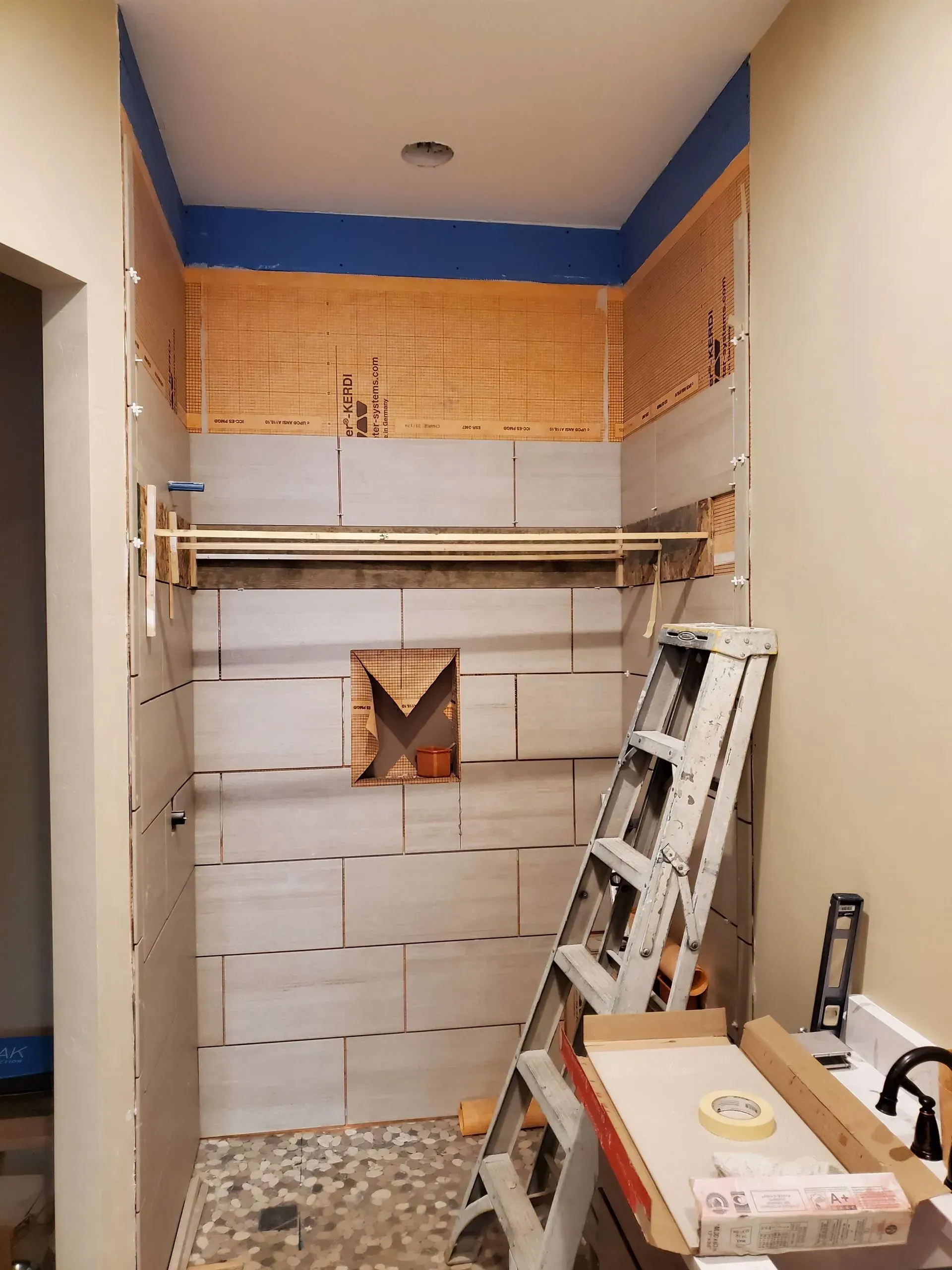 Small unfinished bathroom with tiled wall, exposed ceiling, and a ladder leaning against the right wall.