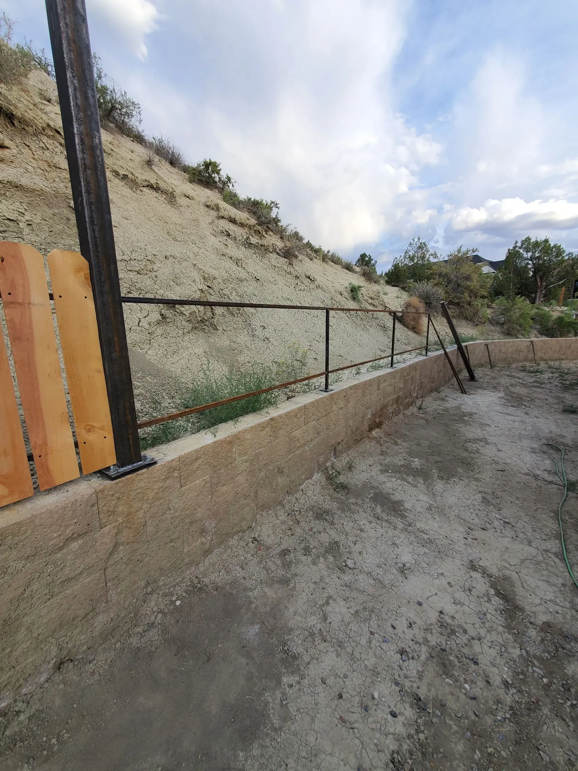Dirt path beside a wire fence and sloped hillside under a cloudy sky