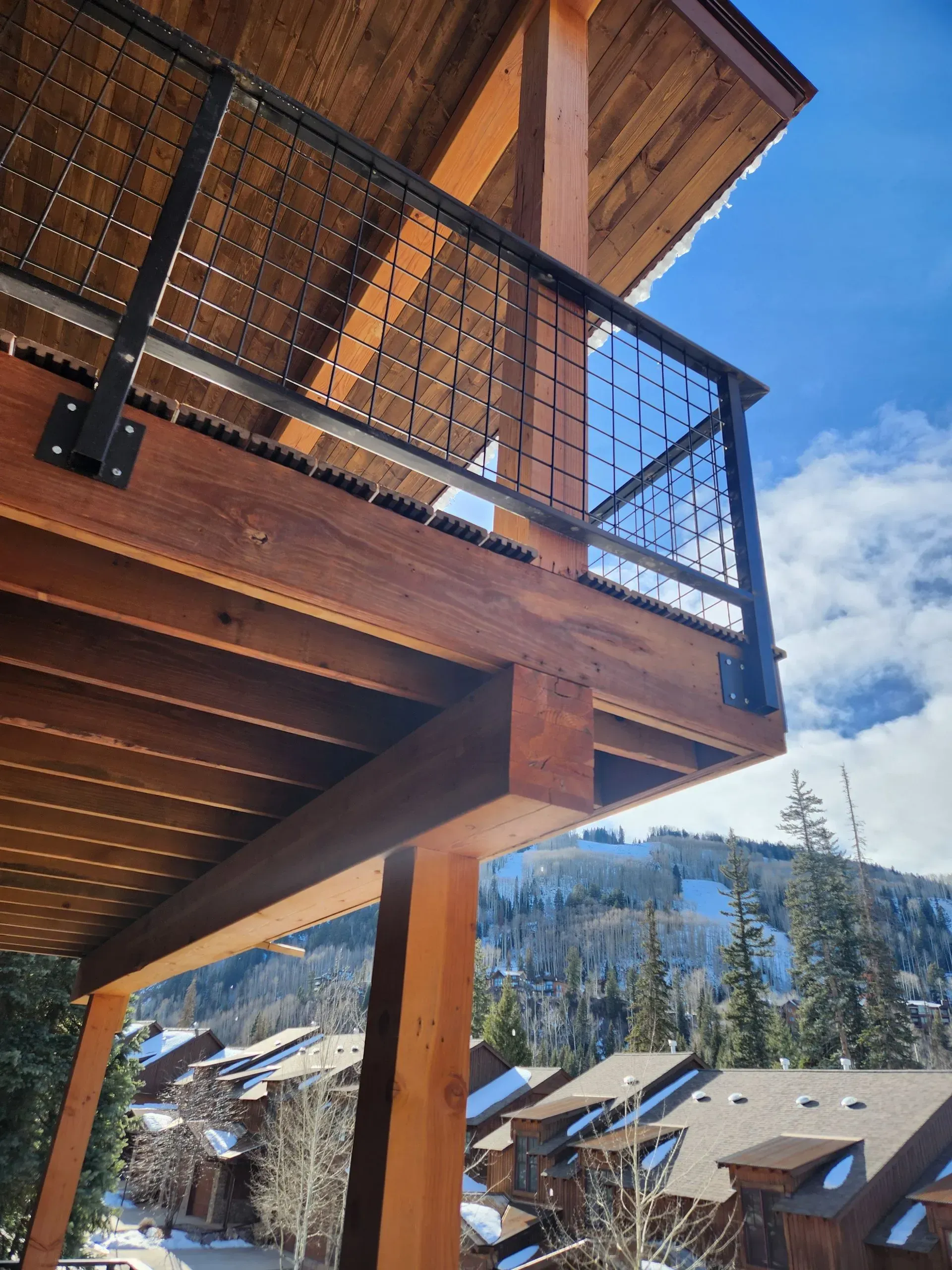 Wooden cabin balcony with metal railing overlooking snowy mountain rooftops under a blue sky
