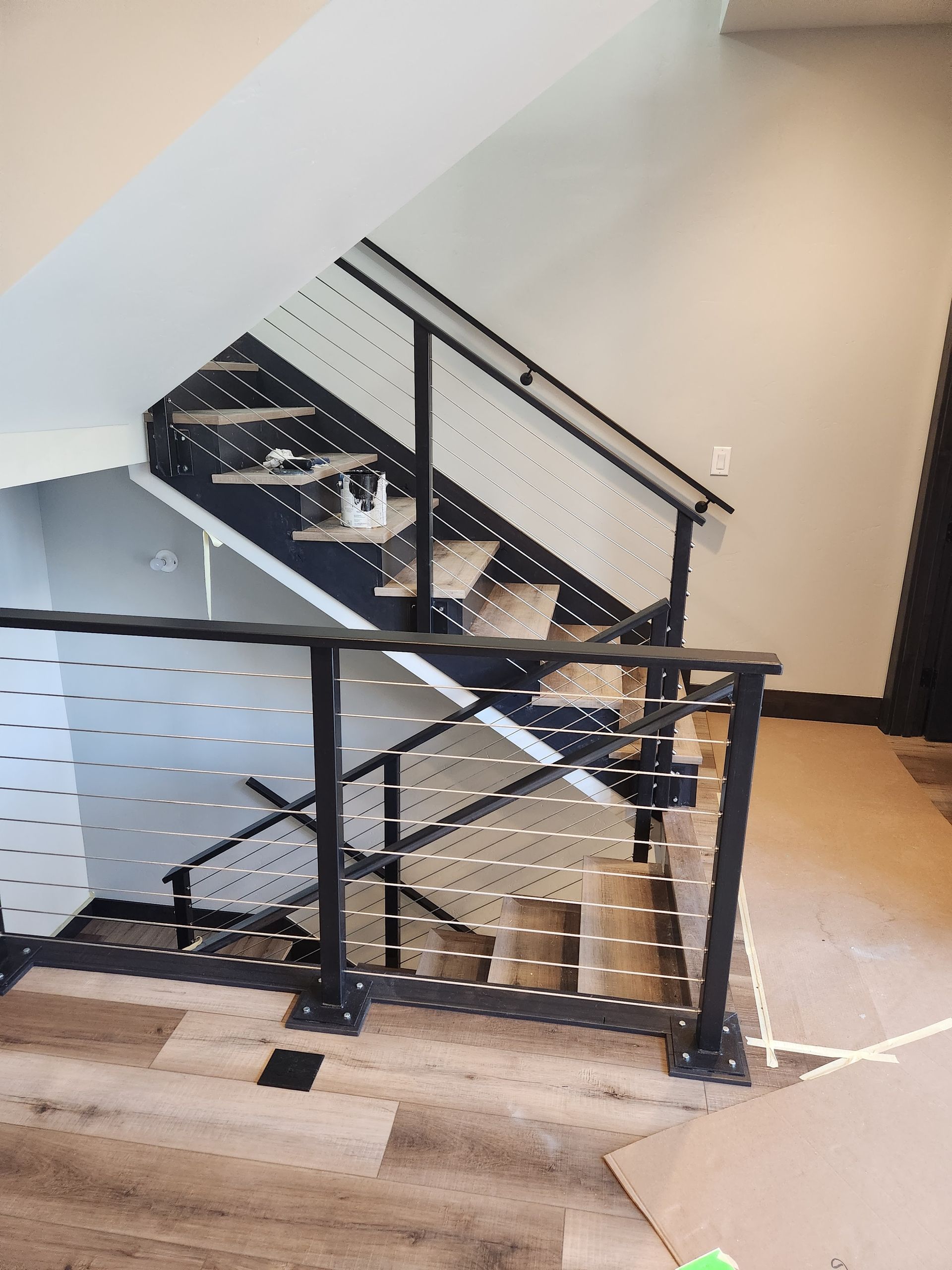 Interior staircase with black railings and white steps beside a wooden floor and landing.