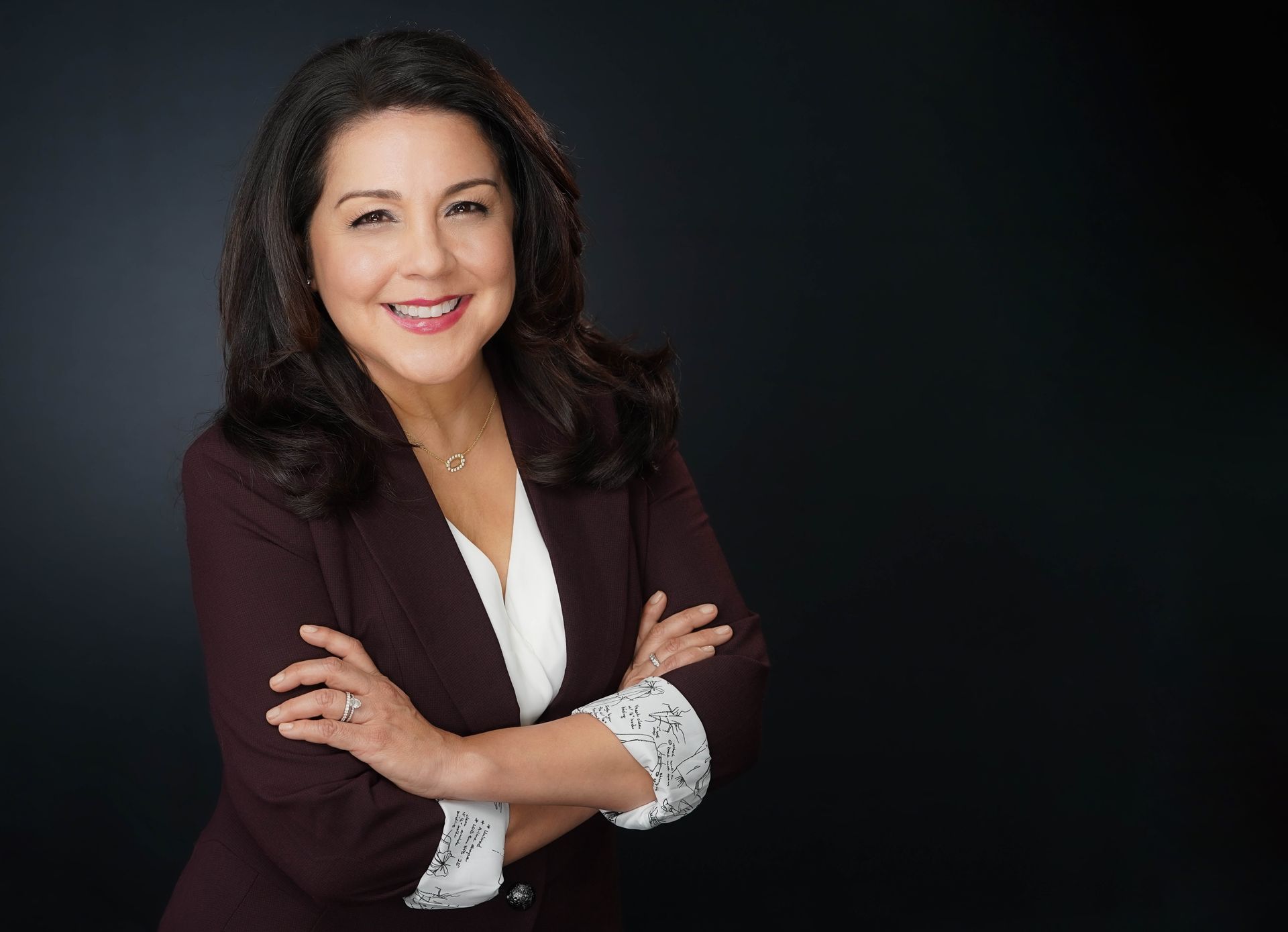 A woman in a business suit is standing with her arms crossed and smiling.