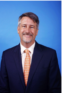 A man in a suit and tie is smiling in front of a blue background