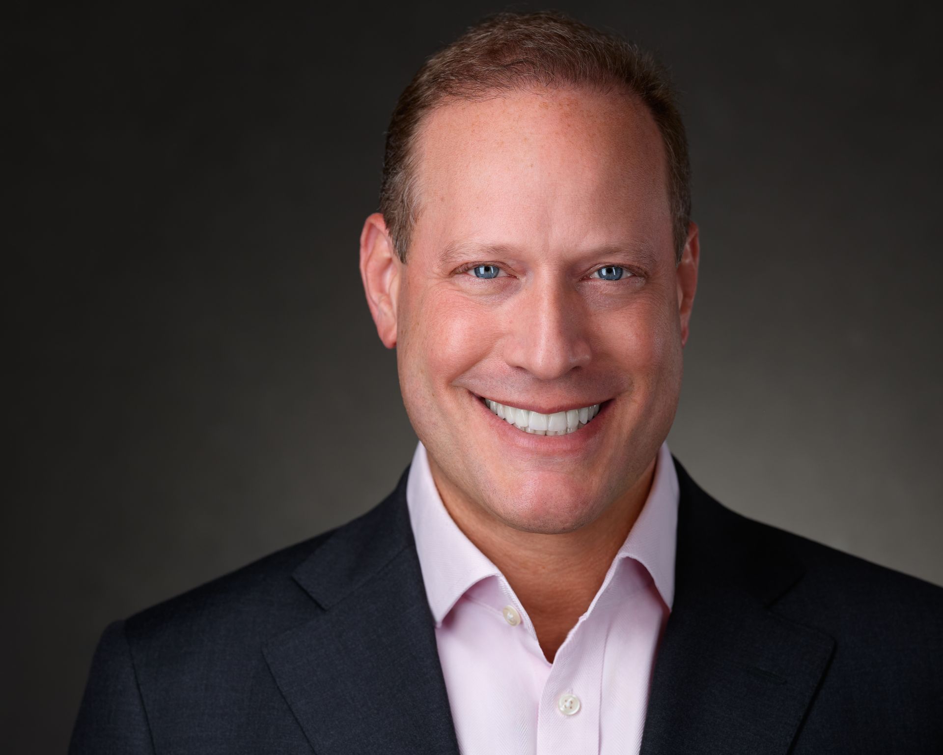 A man in a suit and pink shirt is smiling for the camera.