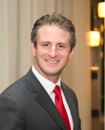 A man in a suit and red tie smiles for the camera