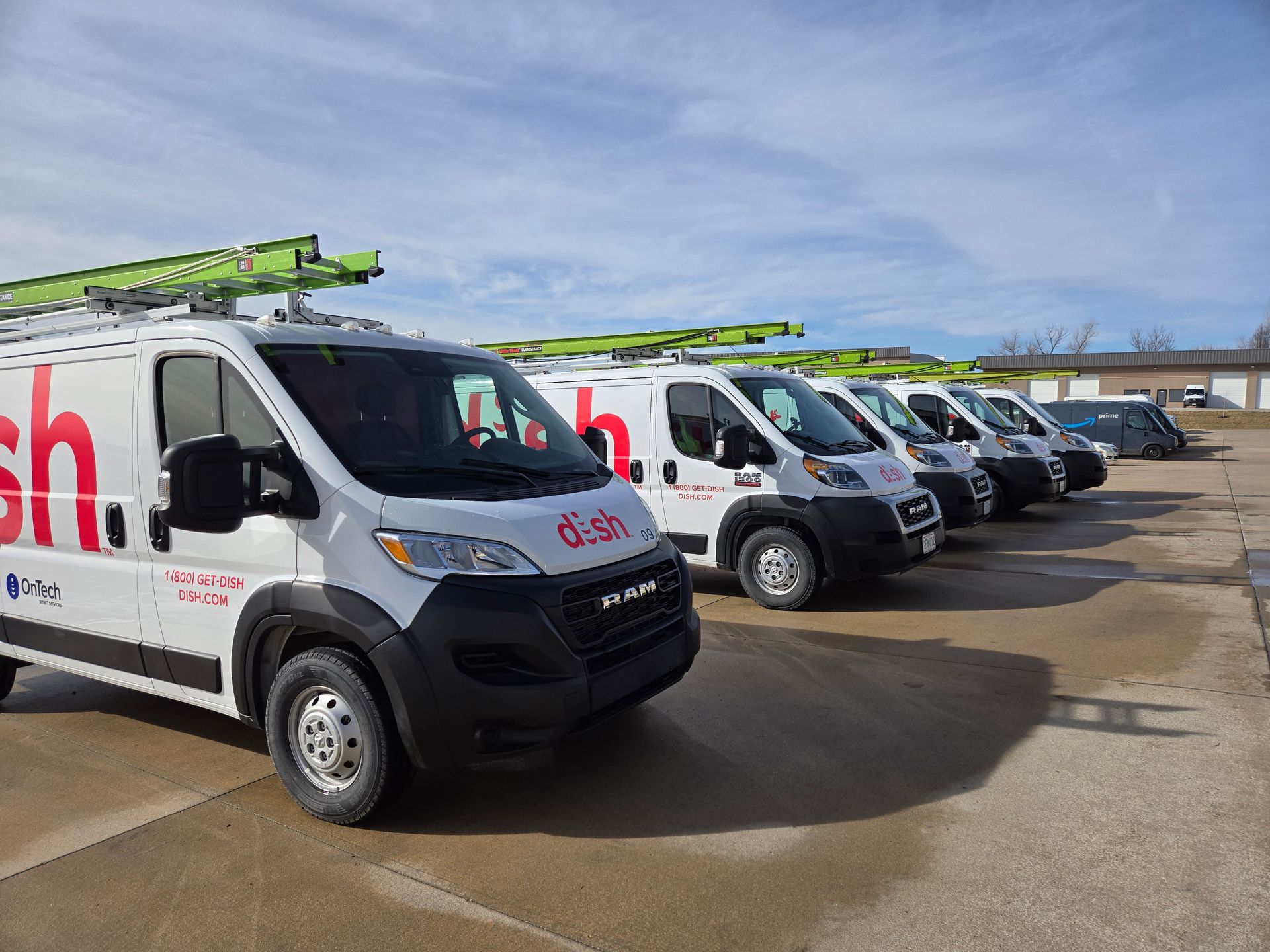 A row of white Dish Network vans parked in a lot under a clear blue sky.