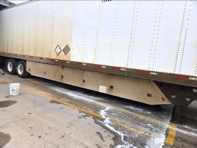 A large white trailer parked on concrete with a white soapy substance leaking onto the ground from underneath it.