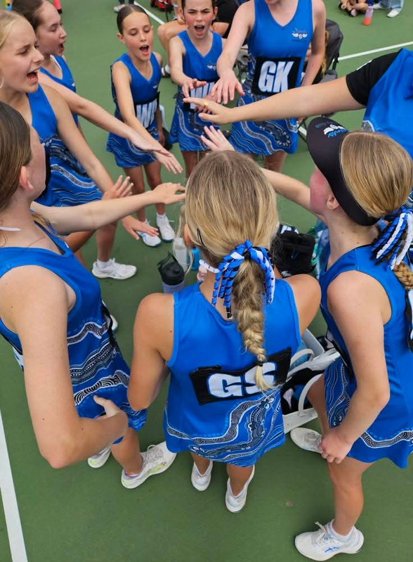 Cheer team in blue uniforms huddles with hands stacked in a pregame circle on a gym floor