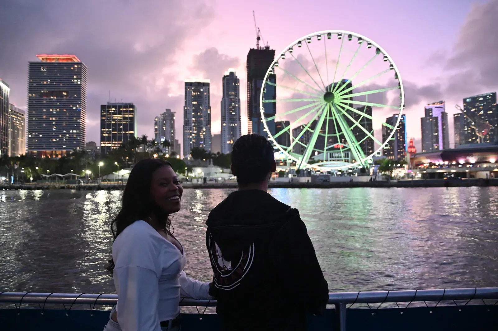 Couple enjoying a Miami Sunset Cruise with skyline views and Bayside Ferris wheel at night.