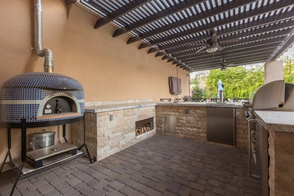 An outdoor kitchen with a pizza oven and a grill under a pergola.