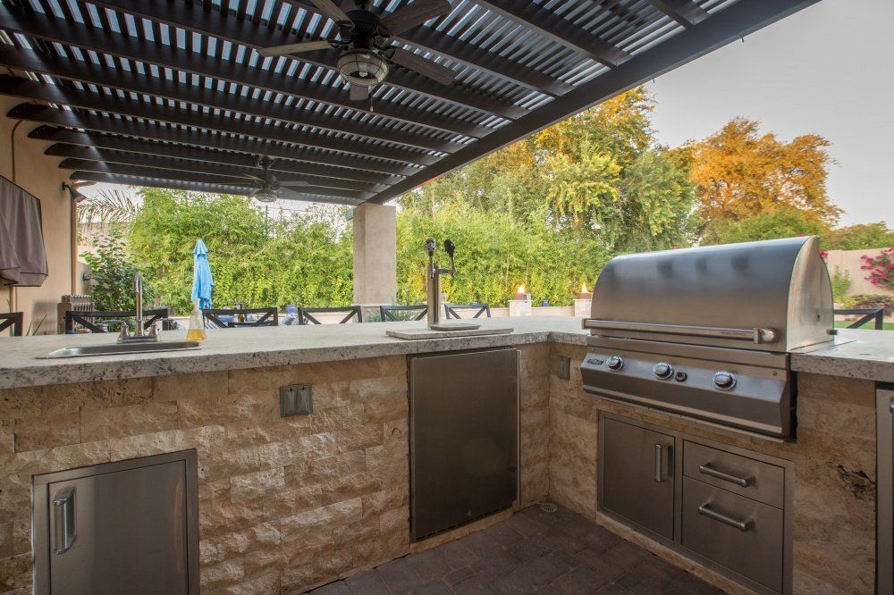 An outdoor kitchen with a grill , sink , and pergola.