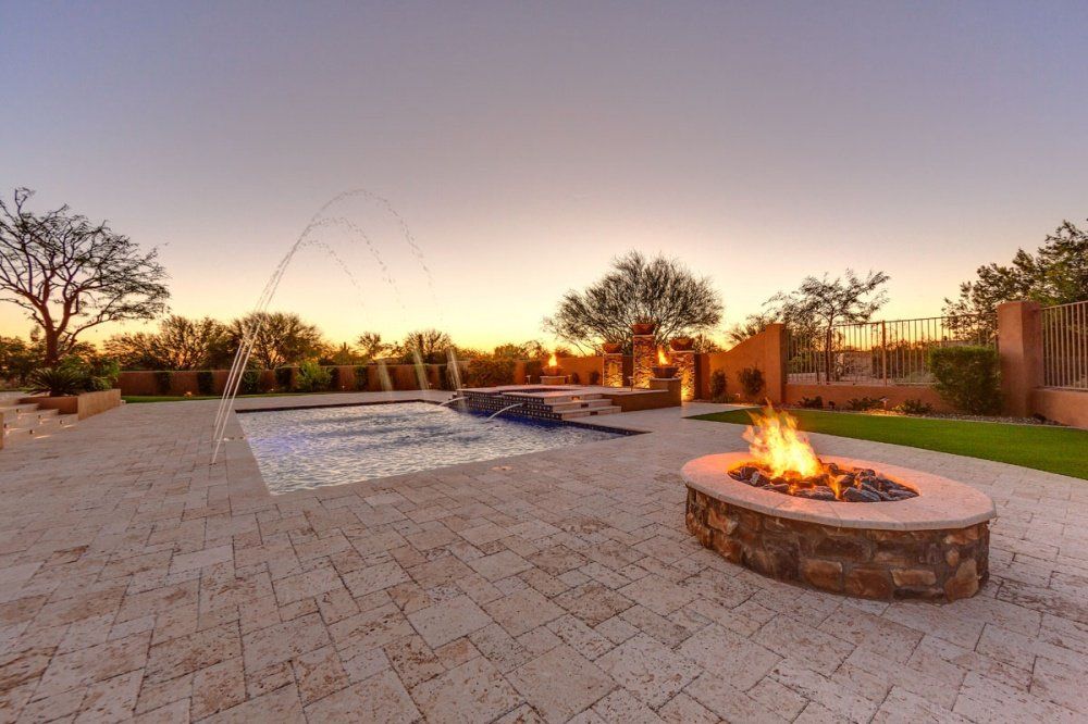 A fire pit is in the middle of a patio next to a pool.