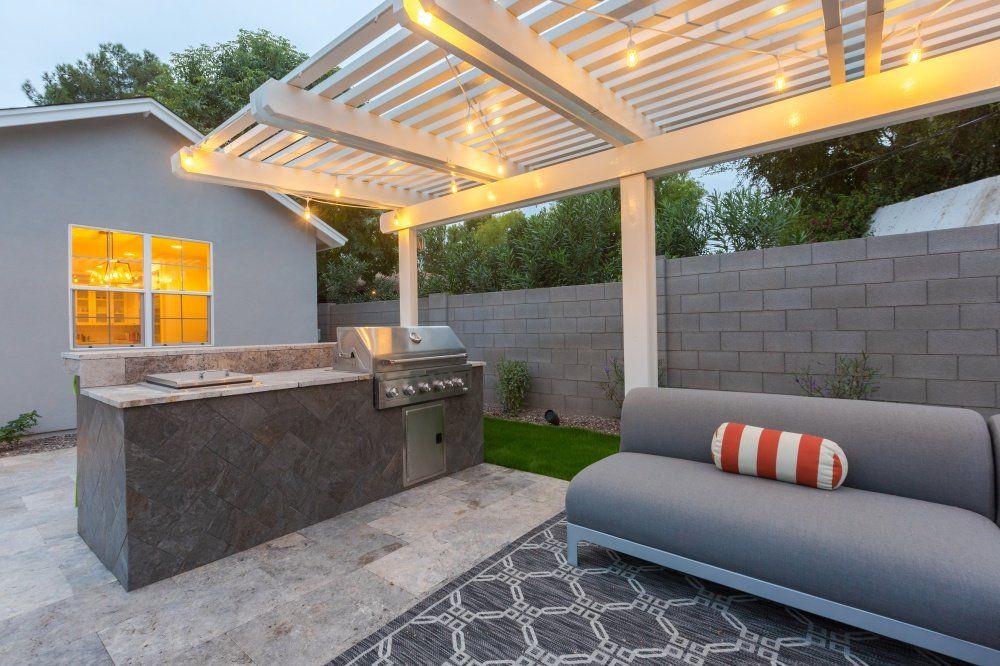 A patio with a grill and a couch under a pergola.