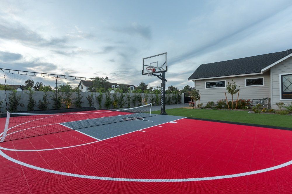 There is a basketball court and a tennis court in the backyard of a house.