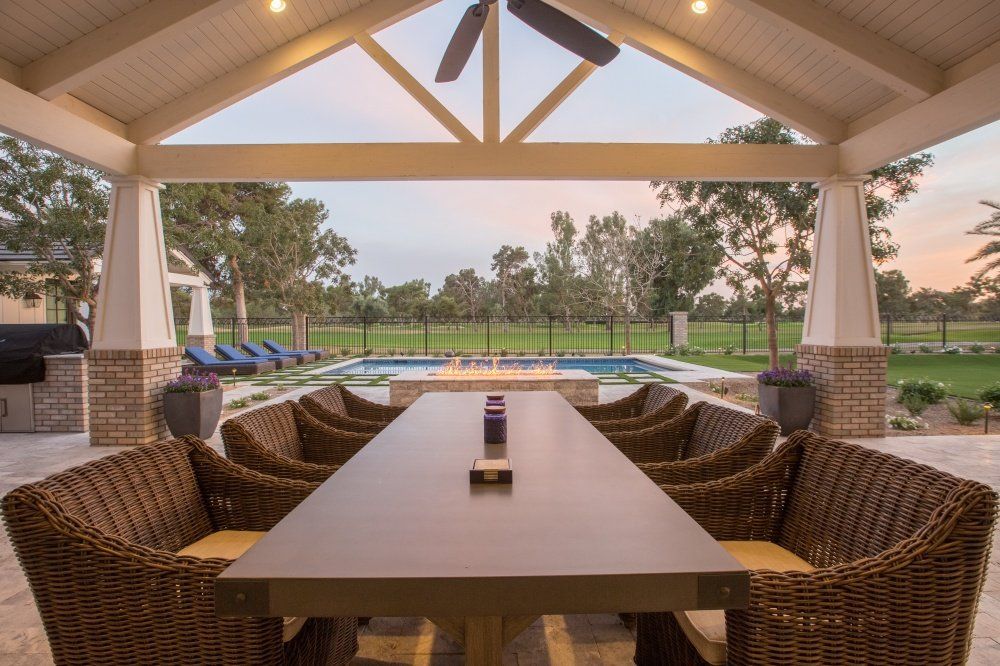 A long table with wicker chairs under a canopy overlooking a pool.