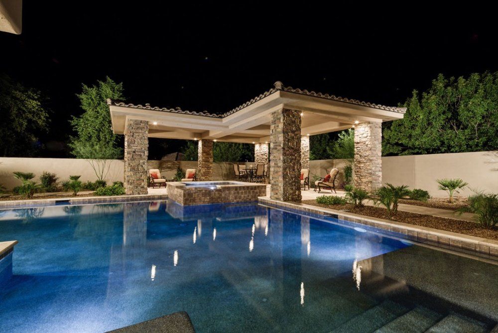 A large swimming pool with a gazebo in the backyard at night