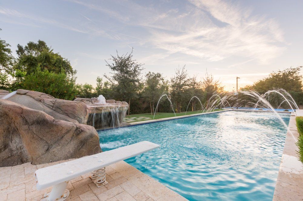 A large swimming pool with a waterfall and a diving board.
