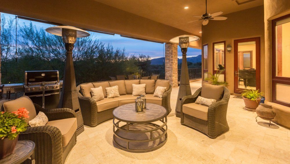 A patio with a couch , chairs , table and heaters.