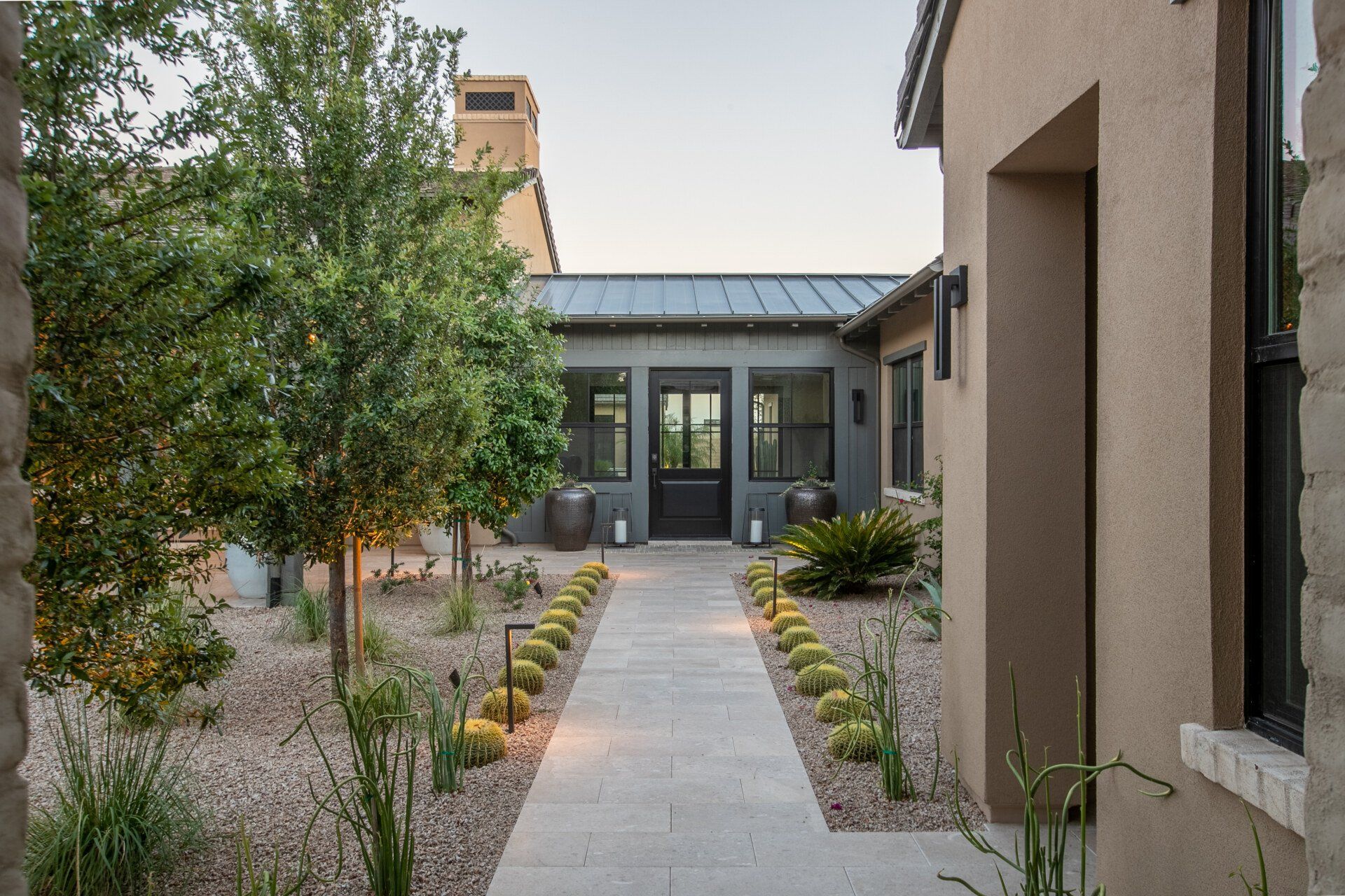 A concrete walkway leading to a house with trees and bushes in front of it.