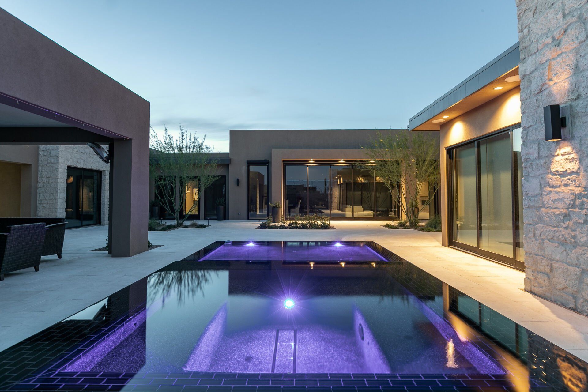 A large swimming pool with purple lights in front of a house