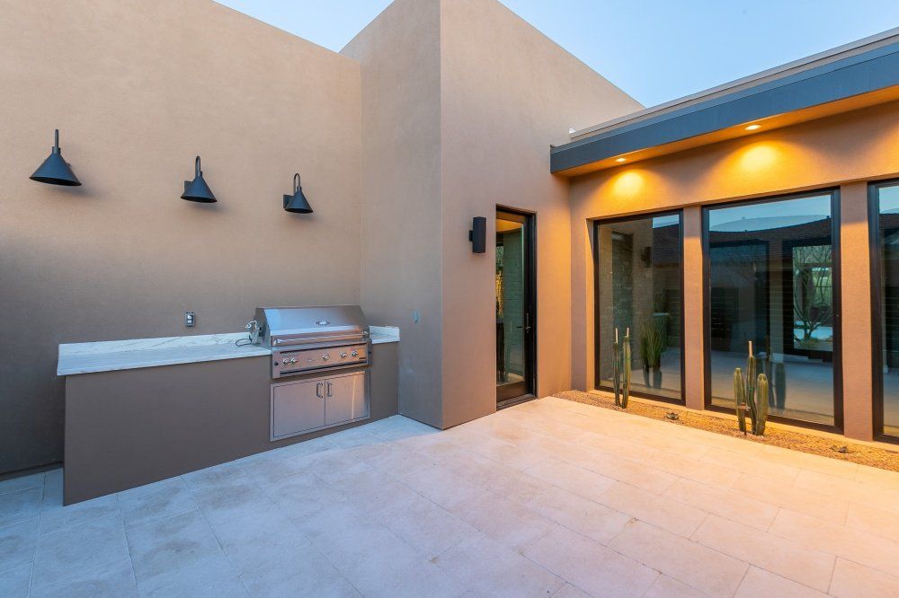 A patio with a grill and a sink in front of a house.