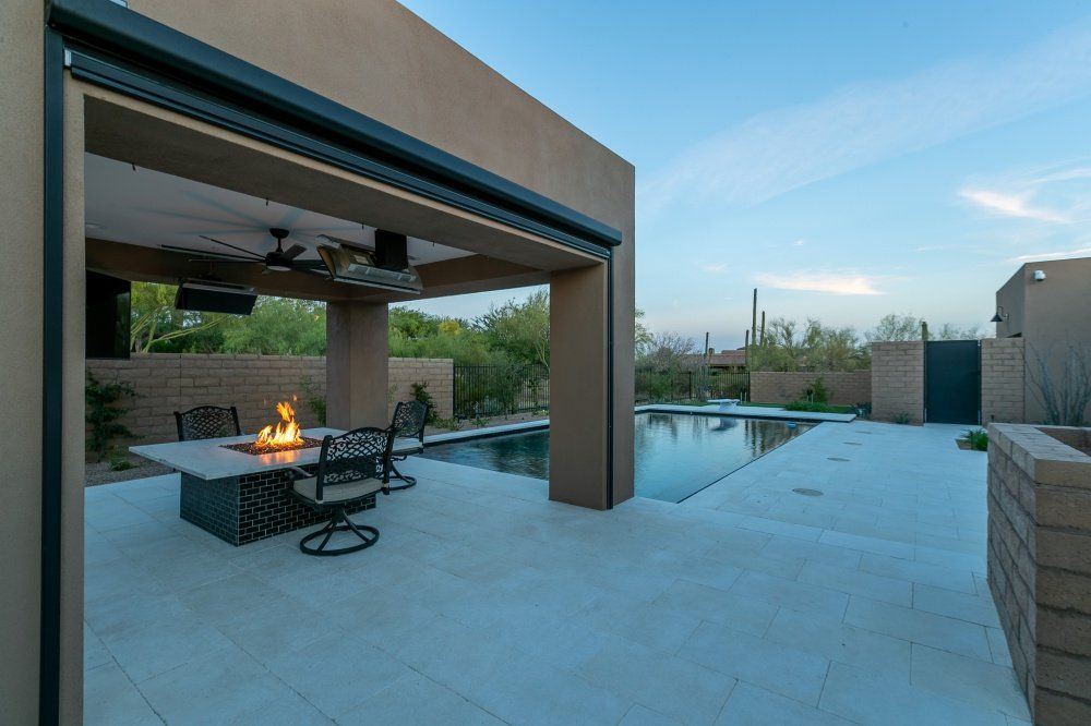 A patio with a table and chairs and a fire pit next to a pool.
