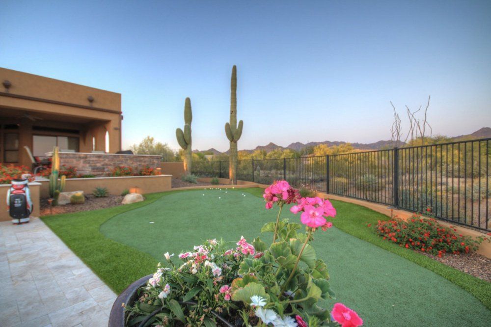 A putting green with flowers in front of a house with a cactus in the background.