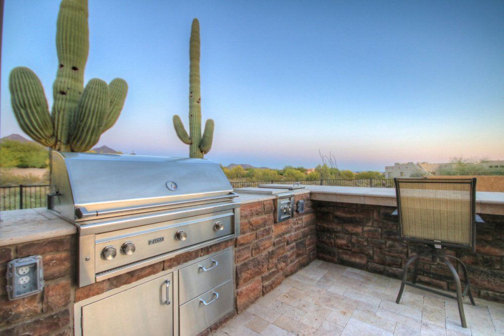 A patio with a grill and a cactus in the background.