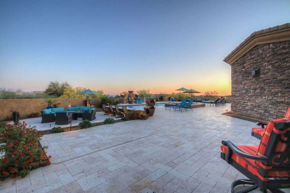 A large patio with chairs and umbrellas and a pool in the background.