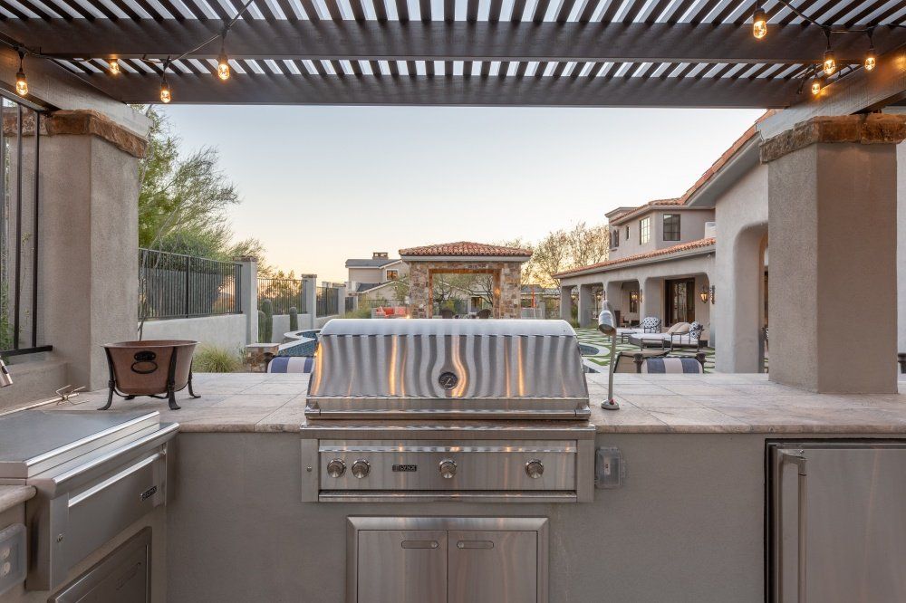 A stainless steel grill is sitting under a pergola in an outdoor kitchen.