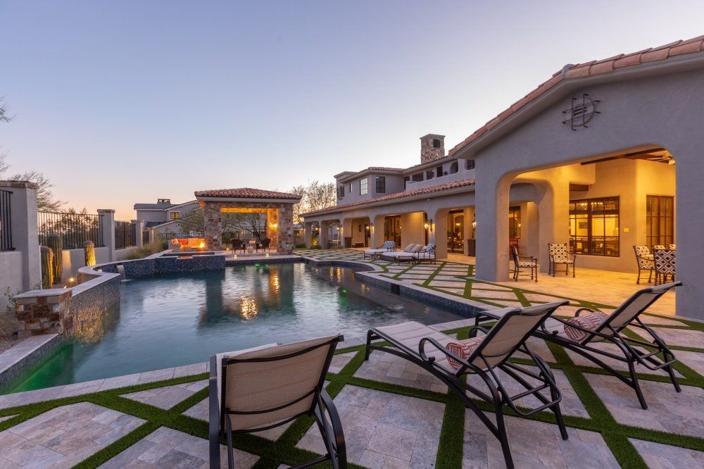 A large house with a swimming pool and chairs in front of it.