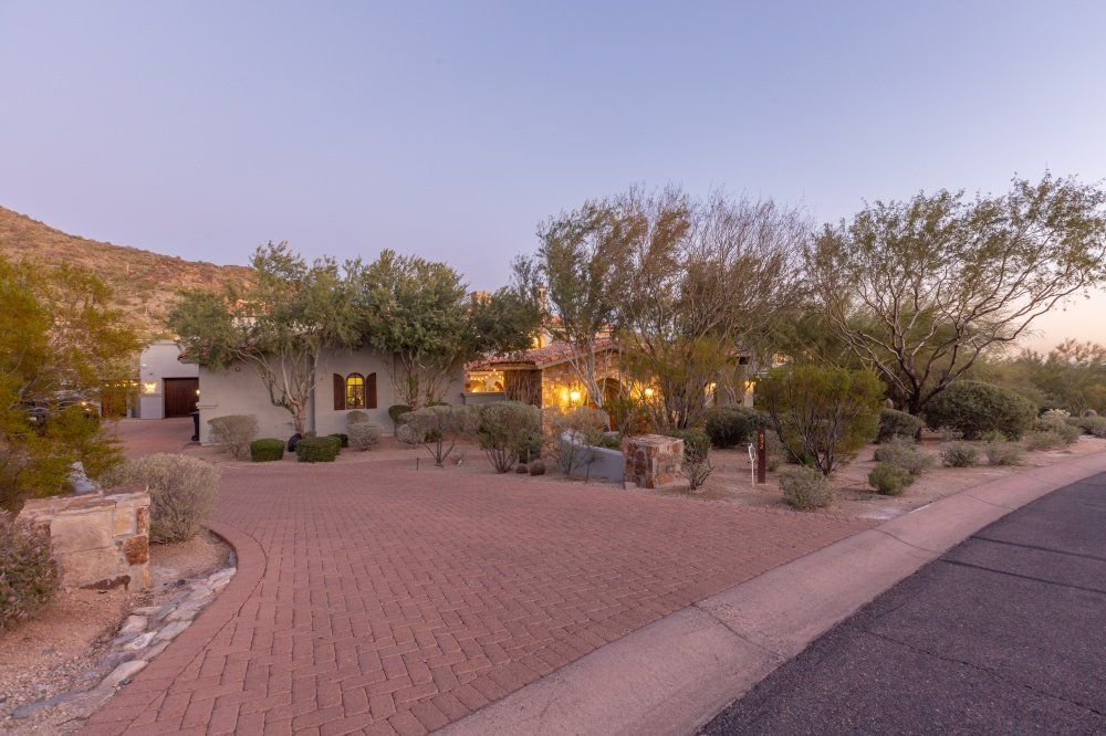 A large house is sitting on top of a hill next to a brick driveway.