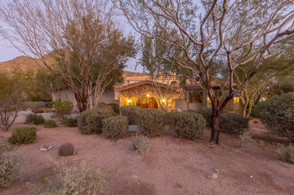 A large house is surrounded by trees and bushes in the desert.
