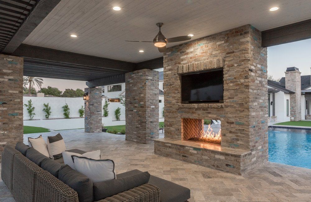 A patio with a fireplace , couch and television.