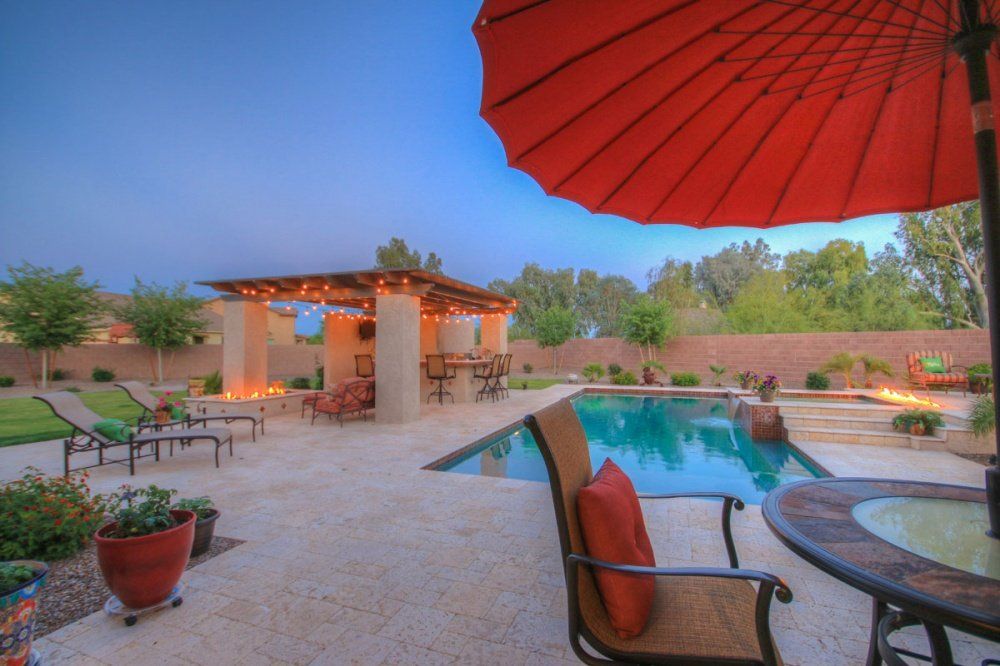 A red umbrella is sitting on a patio next to a pool.