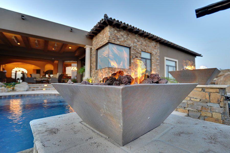 A fire pit in front of a house with a pool in the background