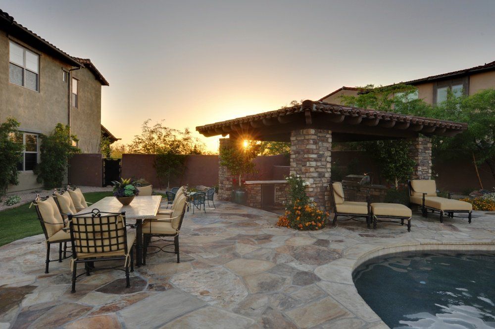 A patio with a table and chairs next to a pool at sunset