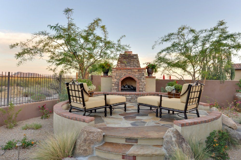There is a fireplace in the middle of the patio with chairs and ottomans.