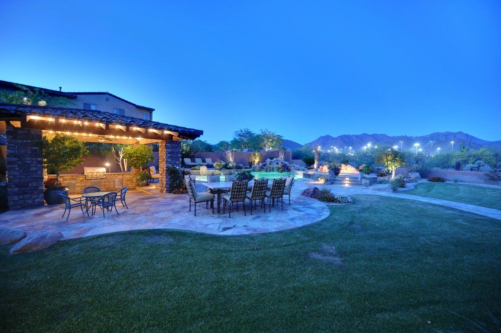 A patio area with a table and chairs in front of a house at night.