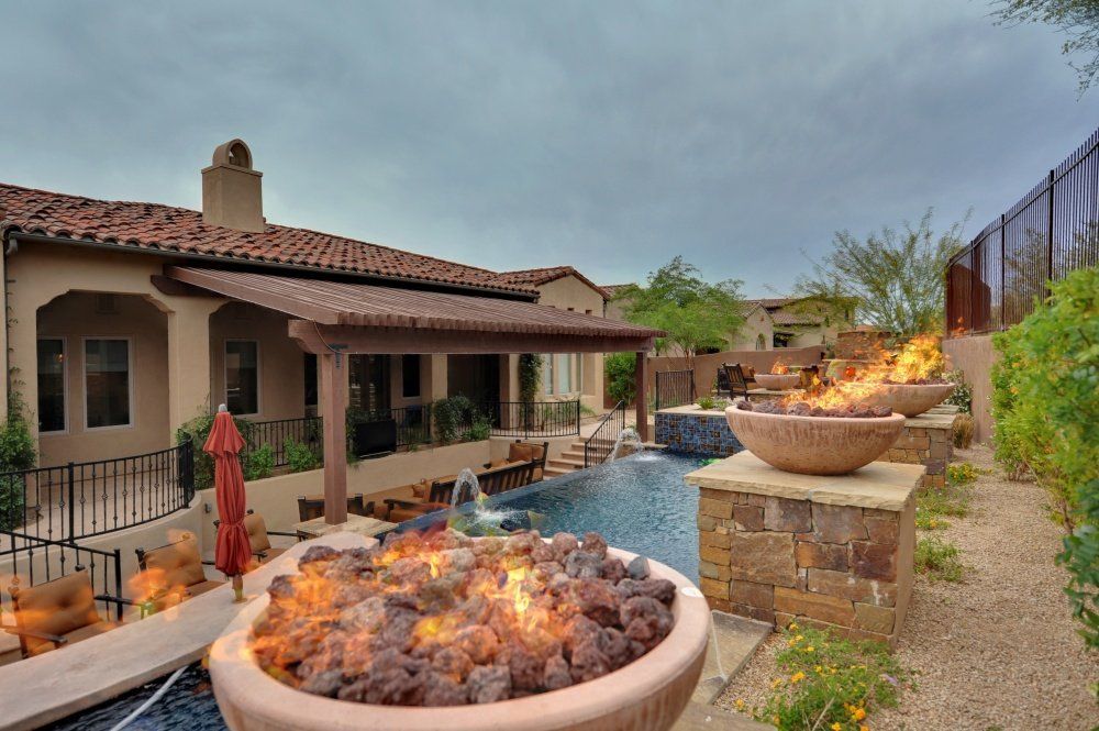 A fire pit in front of a large house next to a pool.