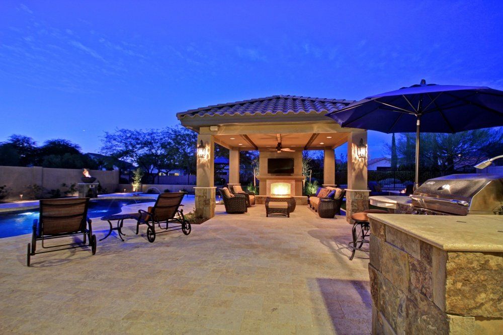 A patio with a gazebo , chairs , umbrellas and a swimming pool at night.