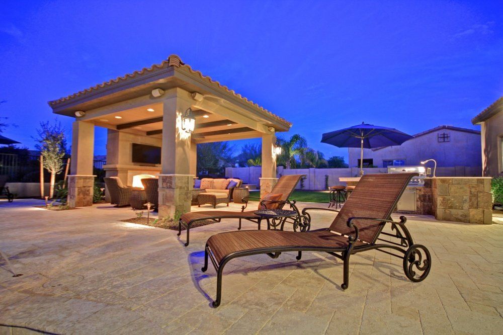 A patio with a gazebo and lounge chairs at night.
