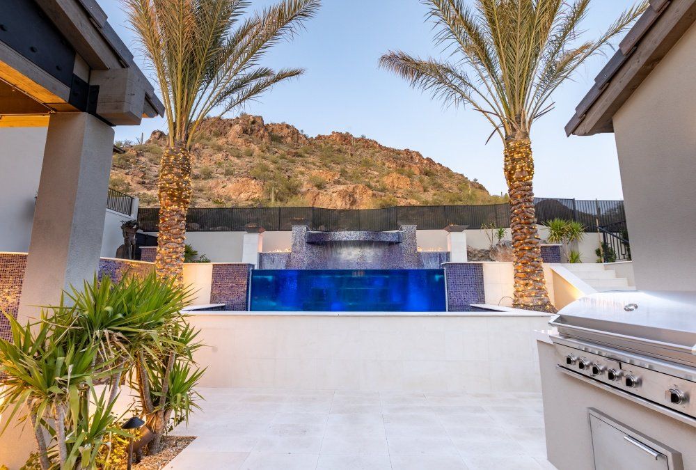 A swimming pool with a waterfall and palm trees in front of a house.