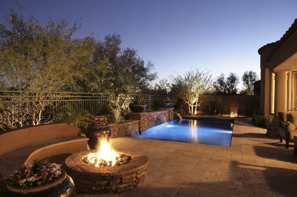 A fire pit is in the middle of a patio next to a pool.