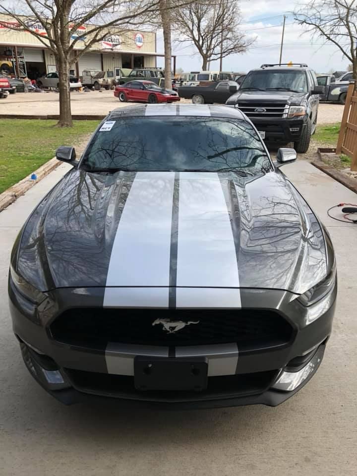 A black mustang with white stripes on the hood is parked in a parking lot.