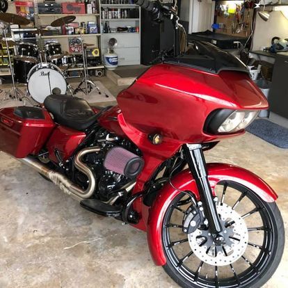 A red motorcycle is parked in a garage next to a drum set.