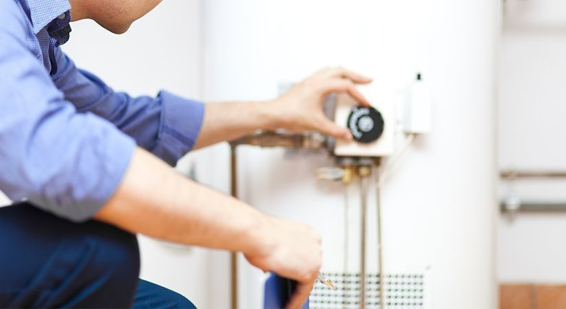 A Man Is Kneeling Down Fixing A Water Heater — Coll Plumbing Pty Ltd in Mackay, QLD