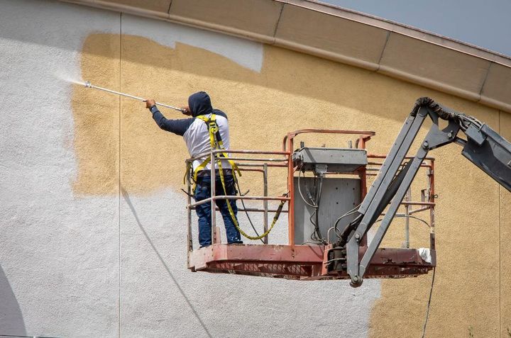 Man painting a yellow wall white using a paint sprayer.