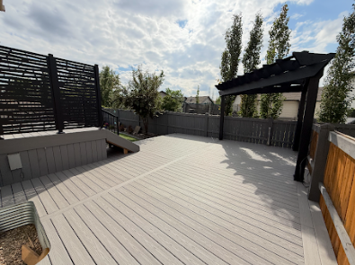 Spacious gray composite deck with black pergola, surrounded by gray fence and a patterned privacy screen.