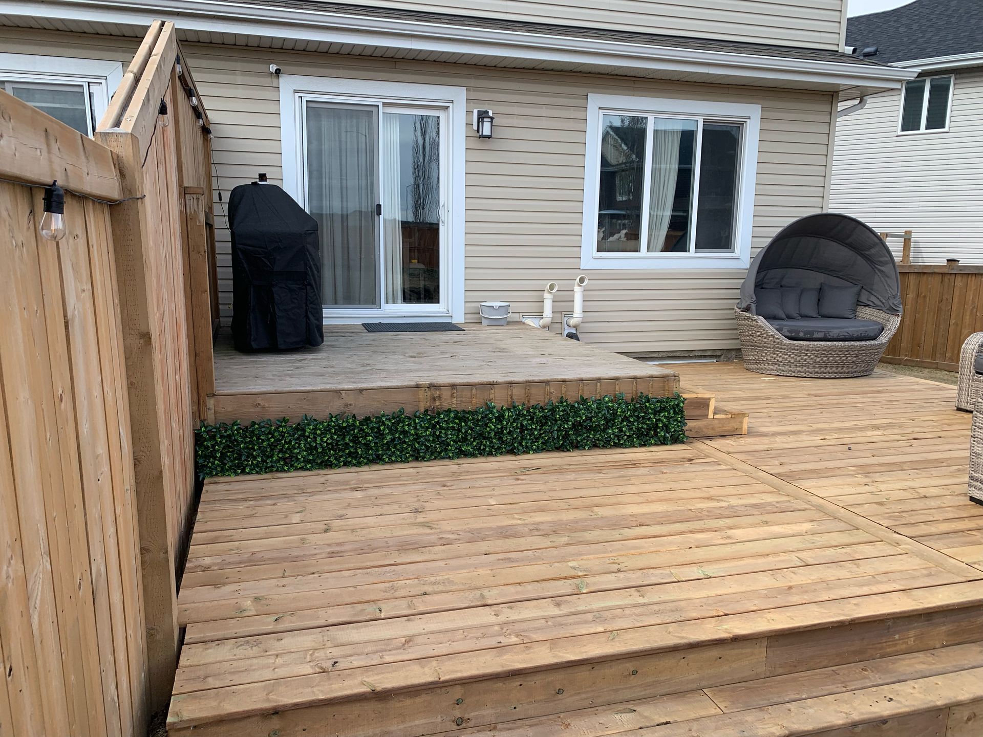 Wooden deck with a covered grill, sliding door, and a round chair.